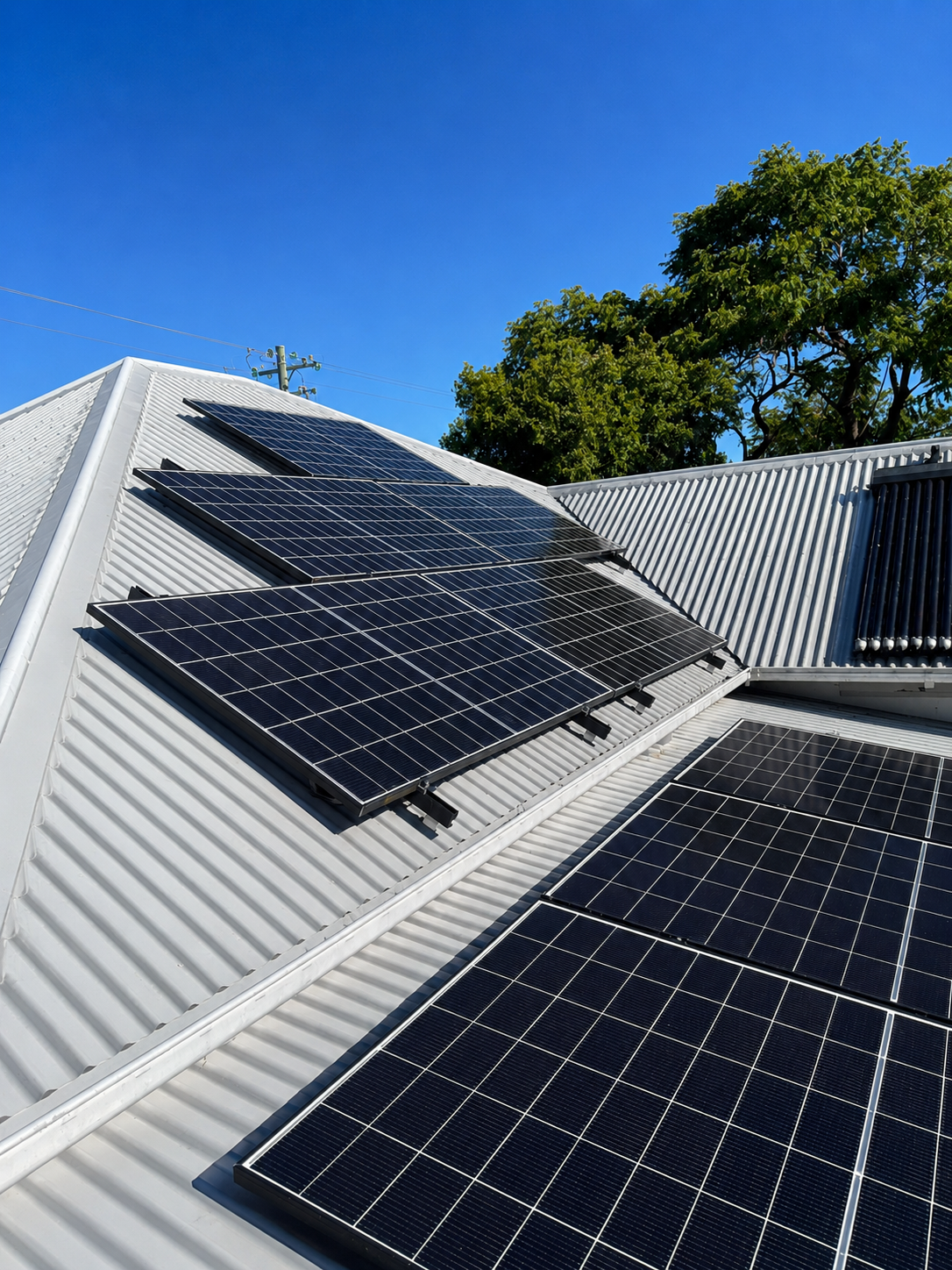 Rooftop solar panels installed on a white corrugated metal roof under clear blue sky